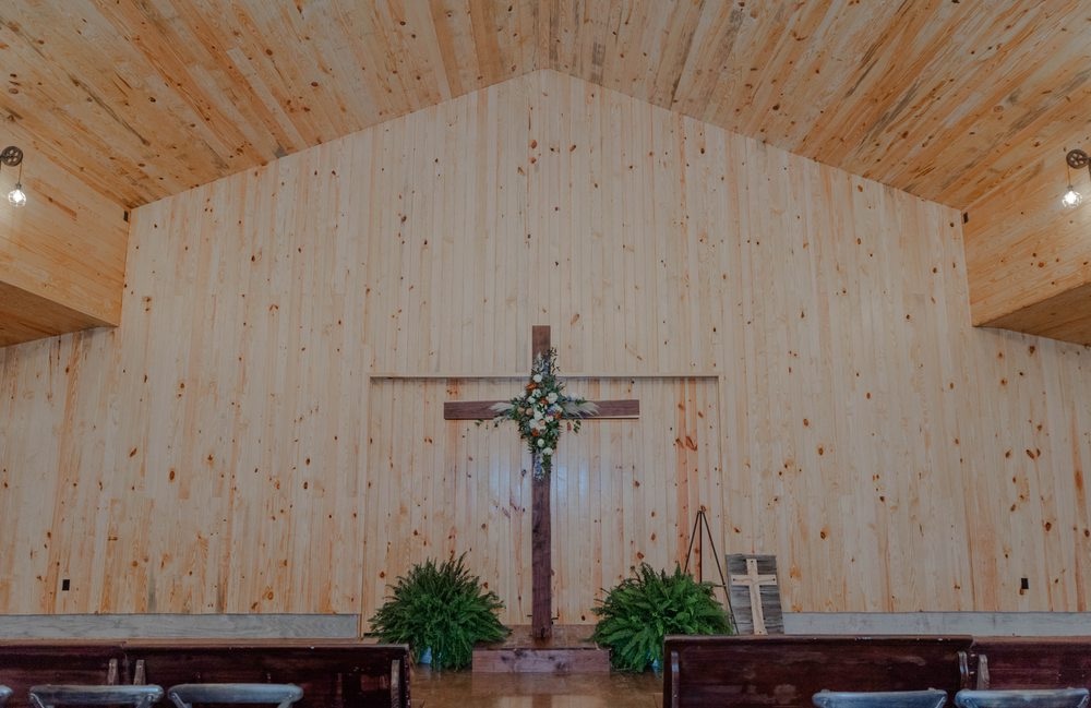 Wooden cross ceremony backdrop with florals inside the Grant Gables barn